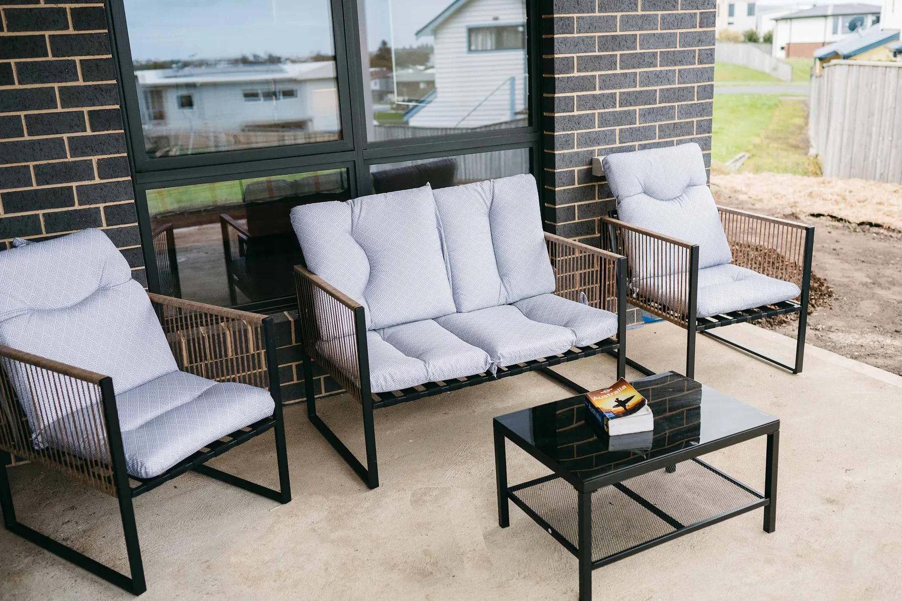 An outdoor patio with cushioned seating and a coffee table beside large windows.