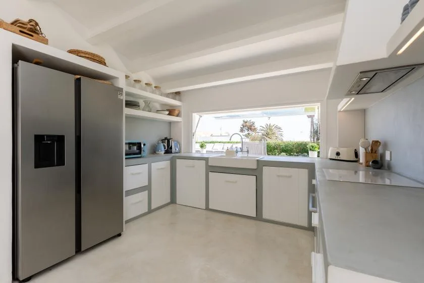 A bright modern kitchen with pale cabinets, stainless steel appliances, and a wide window.