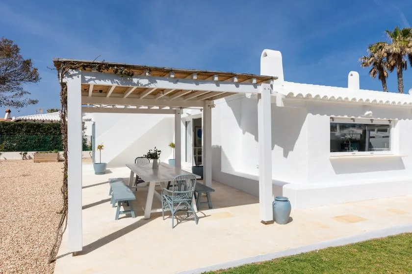 A white patio with a pergola shading an outdoor dining table and seating.