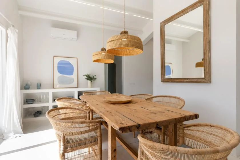 A dining area with a wooden table, woven seating, and hanging pendant lights.