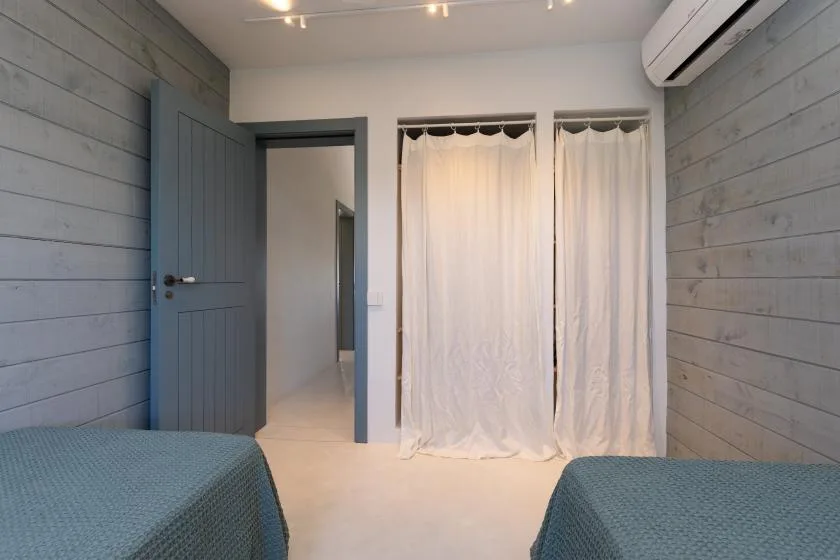 A bedroom with two beds, curtained windows, and an open doorway.