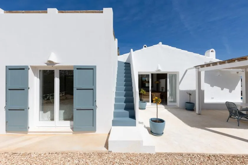 White stucco courtyard with blue shutters, exterior stairs, and a covered patio.