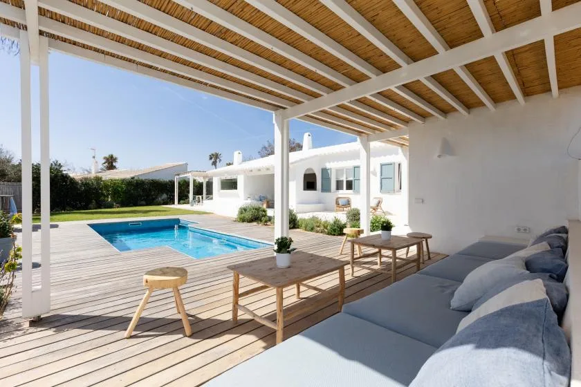 A covered patio with outdoor seating overlooks a swimming pool.