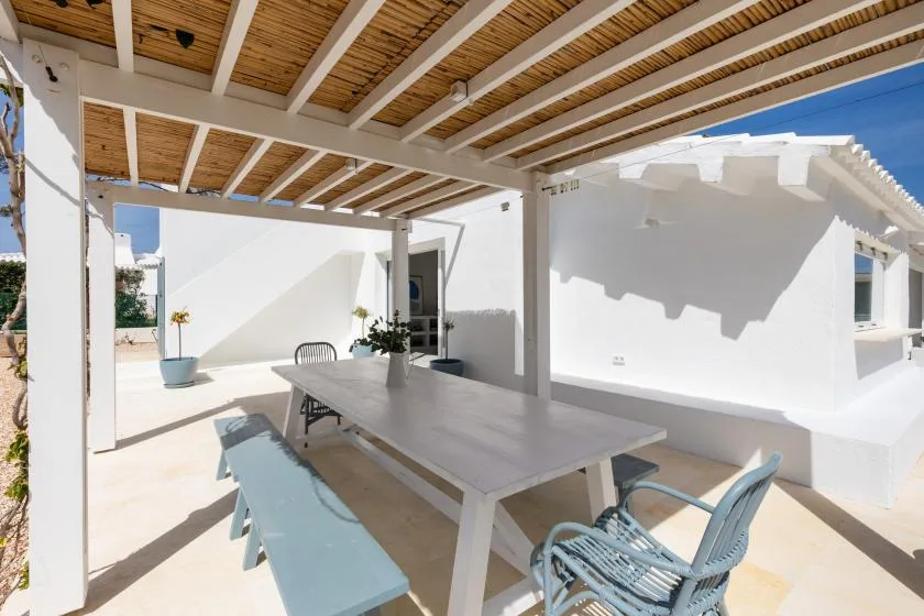 A shaded outdoor dining area beneath a wooden pergola, with a table and seating.