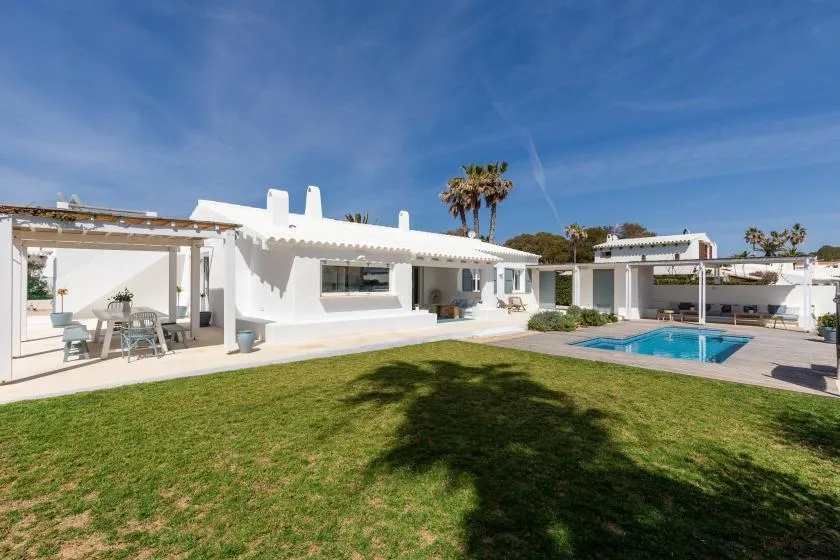 A white modern house faces a lawn, with a swimming pool and covered patio.