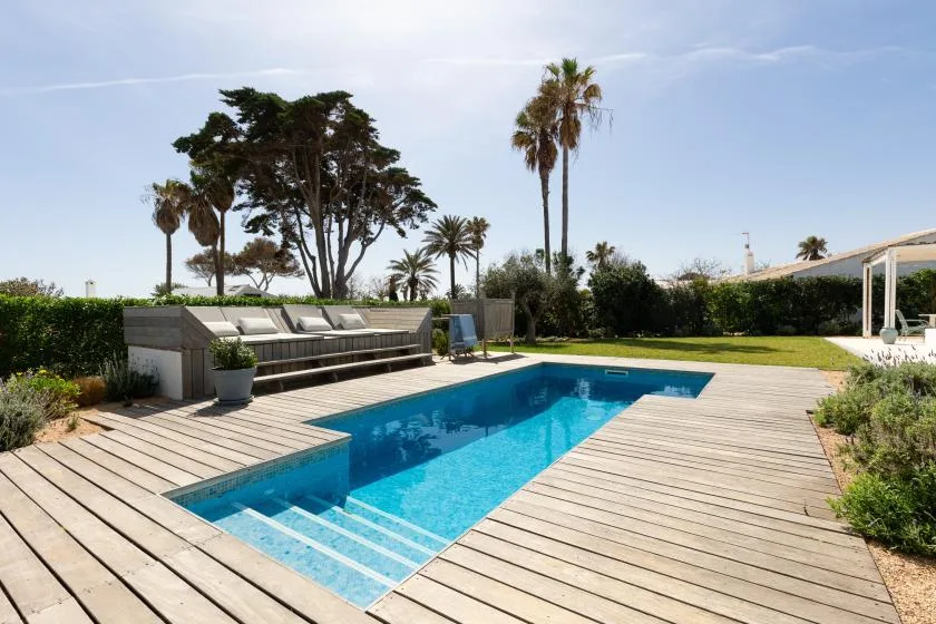 An outdoor swimming pool is surrounded by a wooden deck and garden.