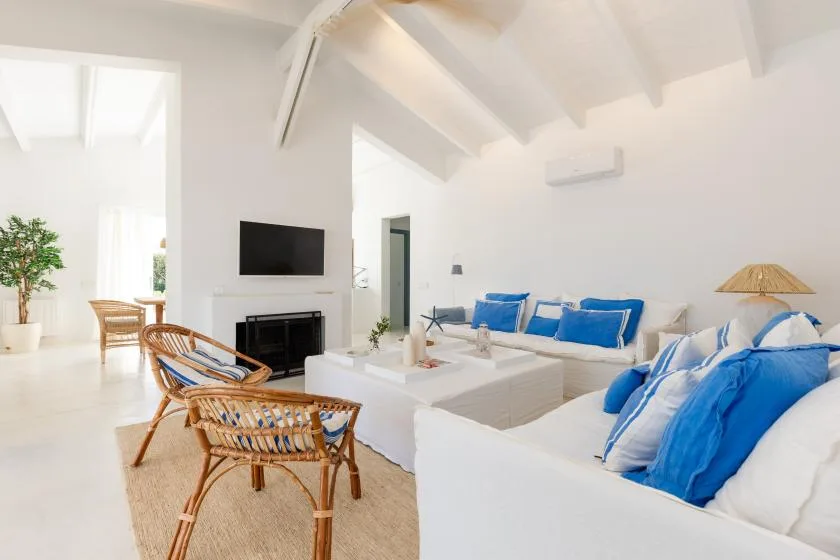 A bright living room with white seating, blue cushions, and a television.