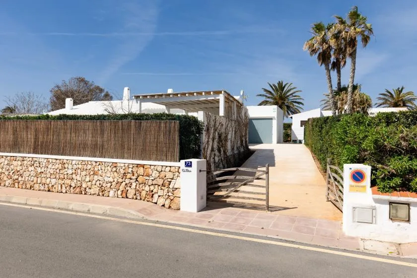 A paved entrance leads past a low stone wall toward a white building.