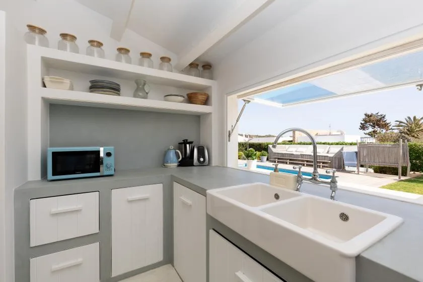 A bright kitchen with a sink, countertop appliances, and a view of the pool outside.