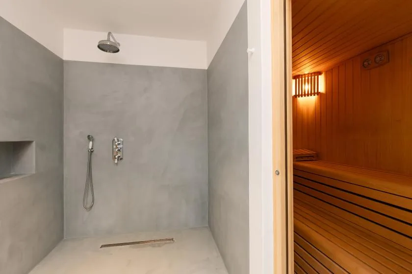 A shower area beside a wood-paneled sauna with bench seating.