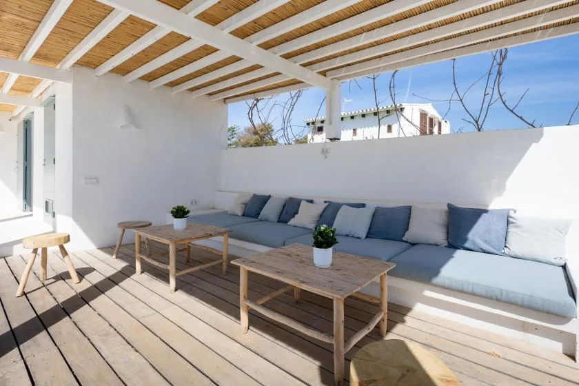 A covered outdoor seating area with a long cushioned bench and wooden tables.
