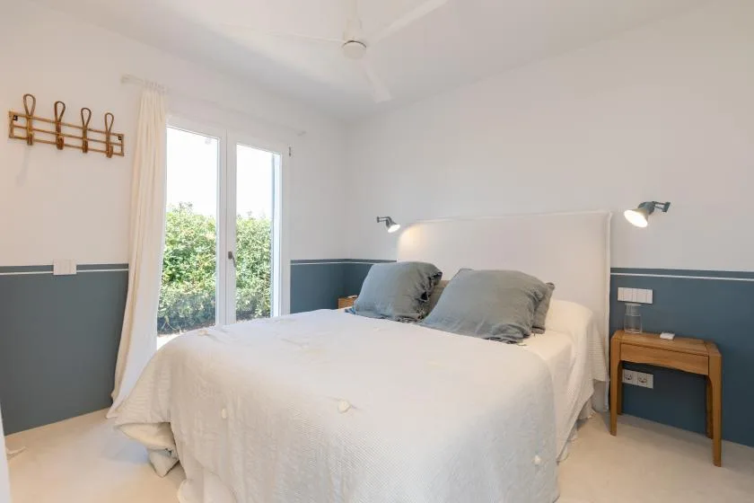 A bright bedroom with a bed and tall windows overlooking greenery.