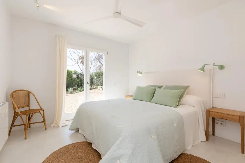 A bright bedroom with a bed, green pillows, and glass doors opening onto a garden.