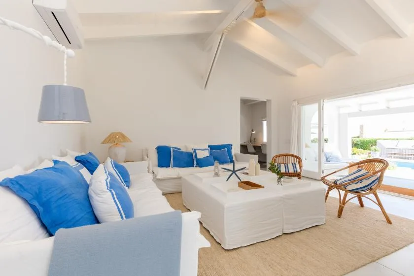 A bright living room with blue cushions, a white coffee table, and doors opening onto a patio.