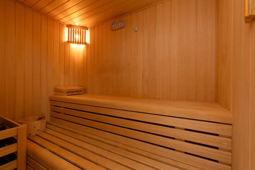 A wood-paneled sauna with tiered wooden seating and a wall light.