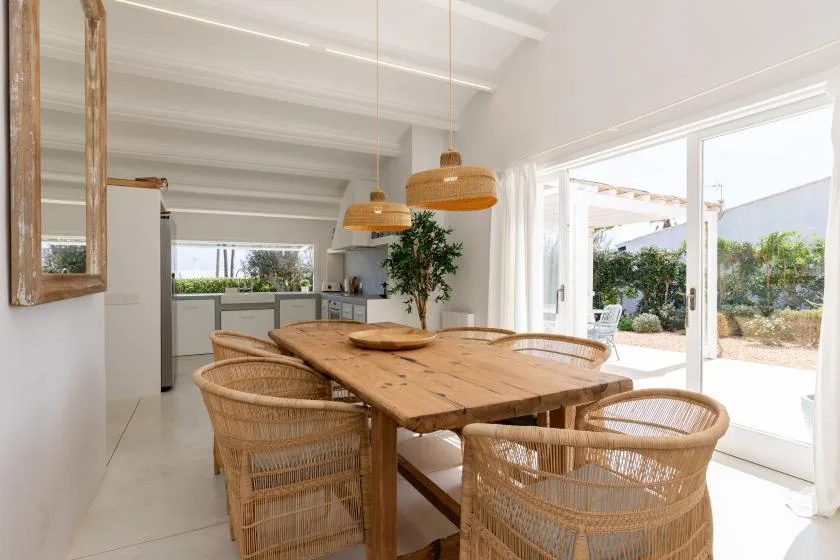 A bright dining area with a wooden table, woven seating, and large glass doors.