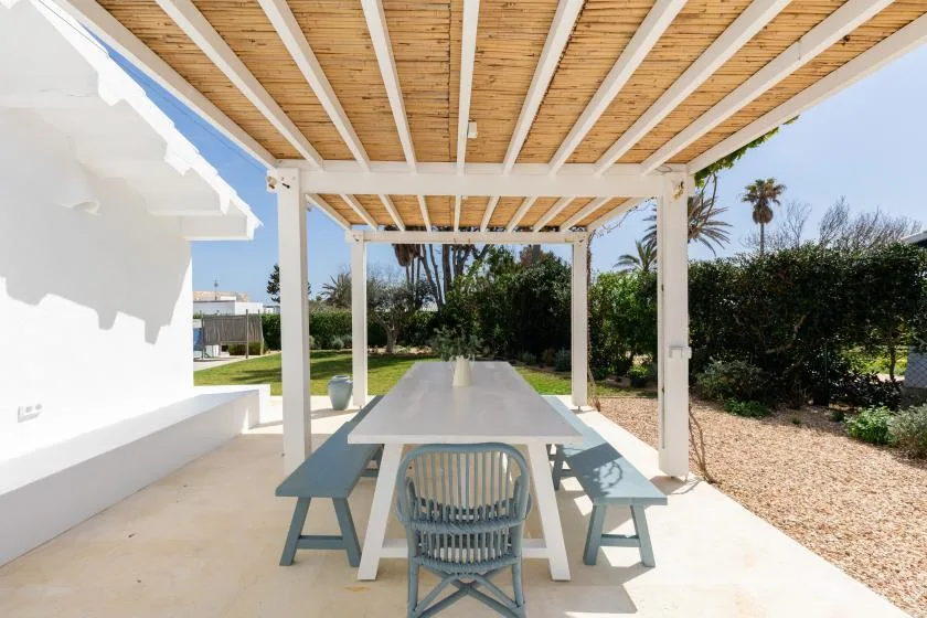 A covered outdoor dining area with a long table and garden views.