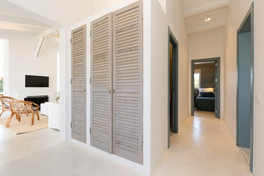 A bright interior hallway with louvered closet doors and a view into a bedroom.