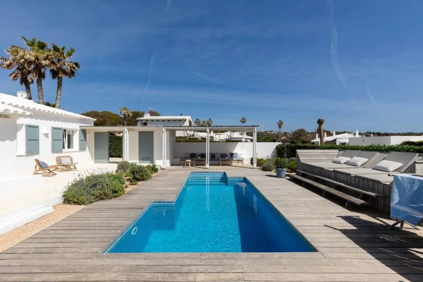 A sunny outdoor pool sits beside a wooden deck and lounge seating.
