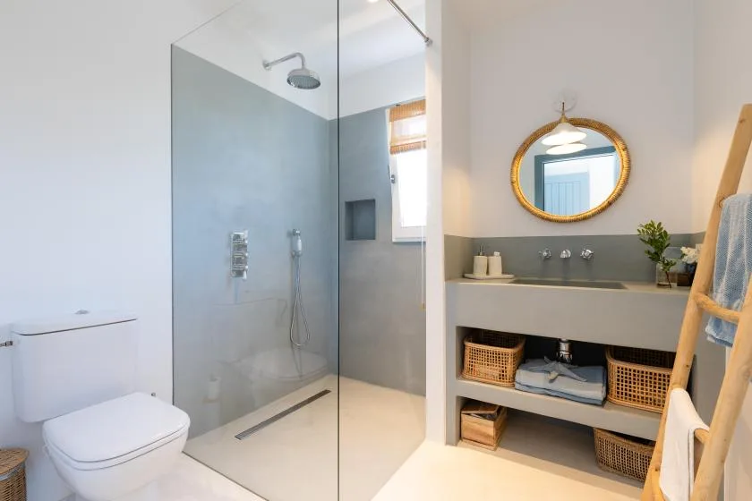 A bright bathroom with a glass shower and a vanity beneath a round mirror.