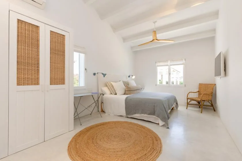 A bright bedroom with a bed, woven rug, and windows.