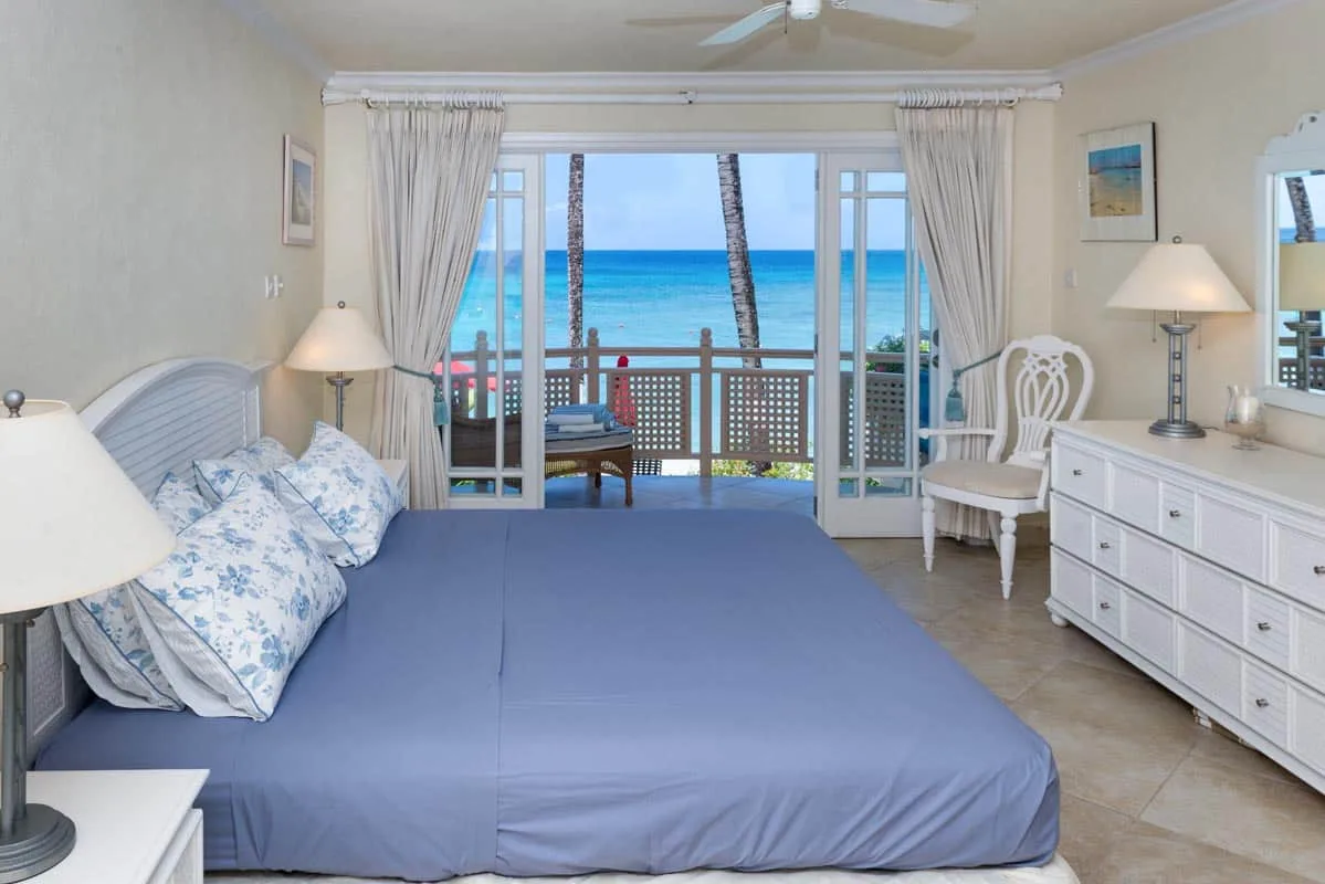 A bedroom with a large bed facing sliding doors that open onto an ocean view.