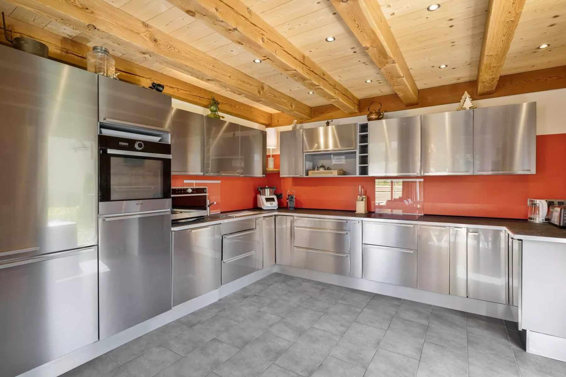 A modern kitchen with stainless steel cabinets, appliances, and a red backsplash.