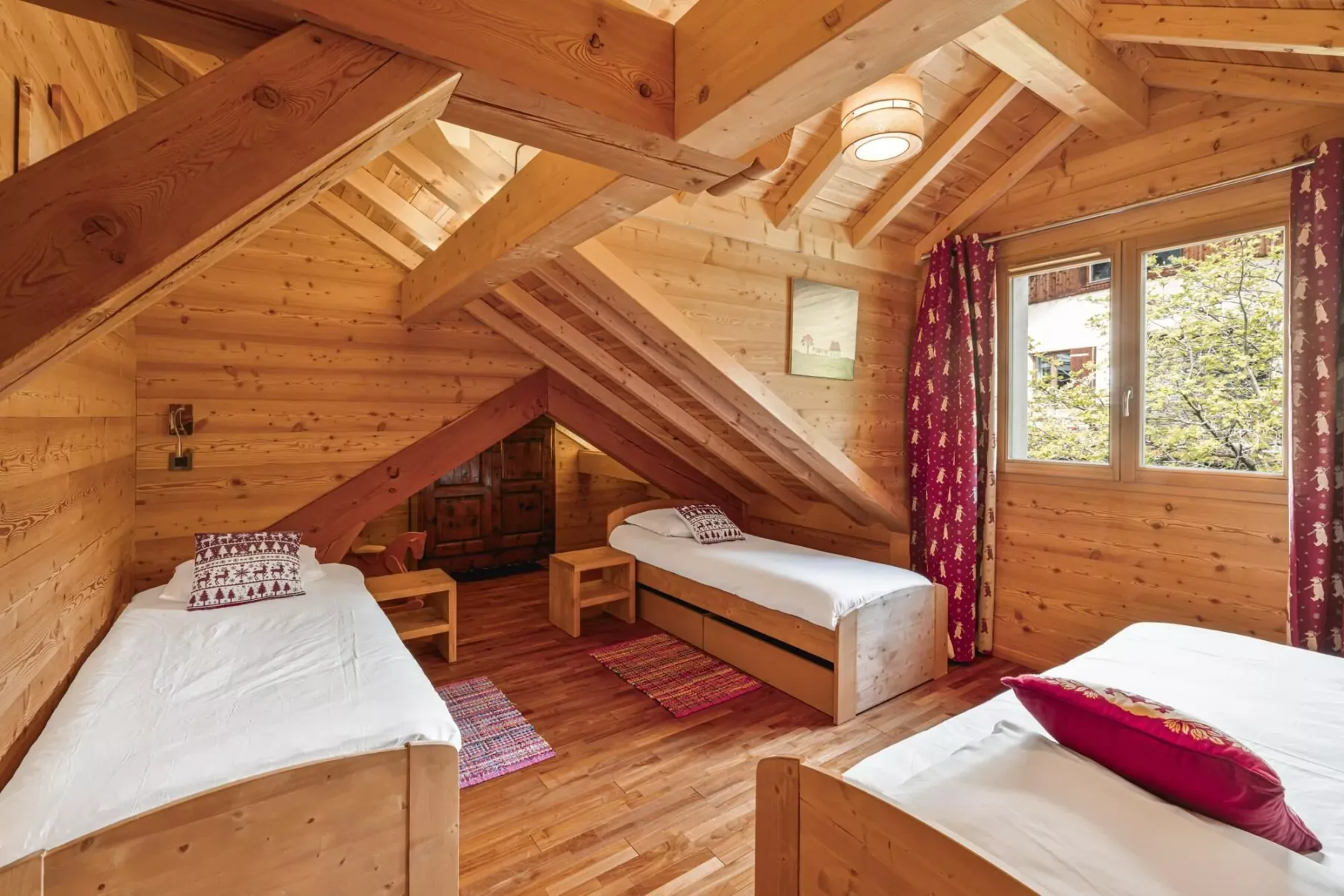 A wood-paneled attic bedroom with beds and a window overlooking trees.