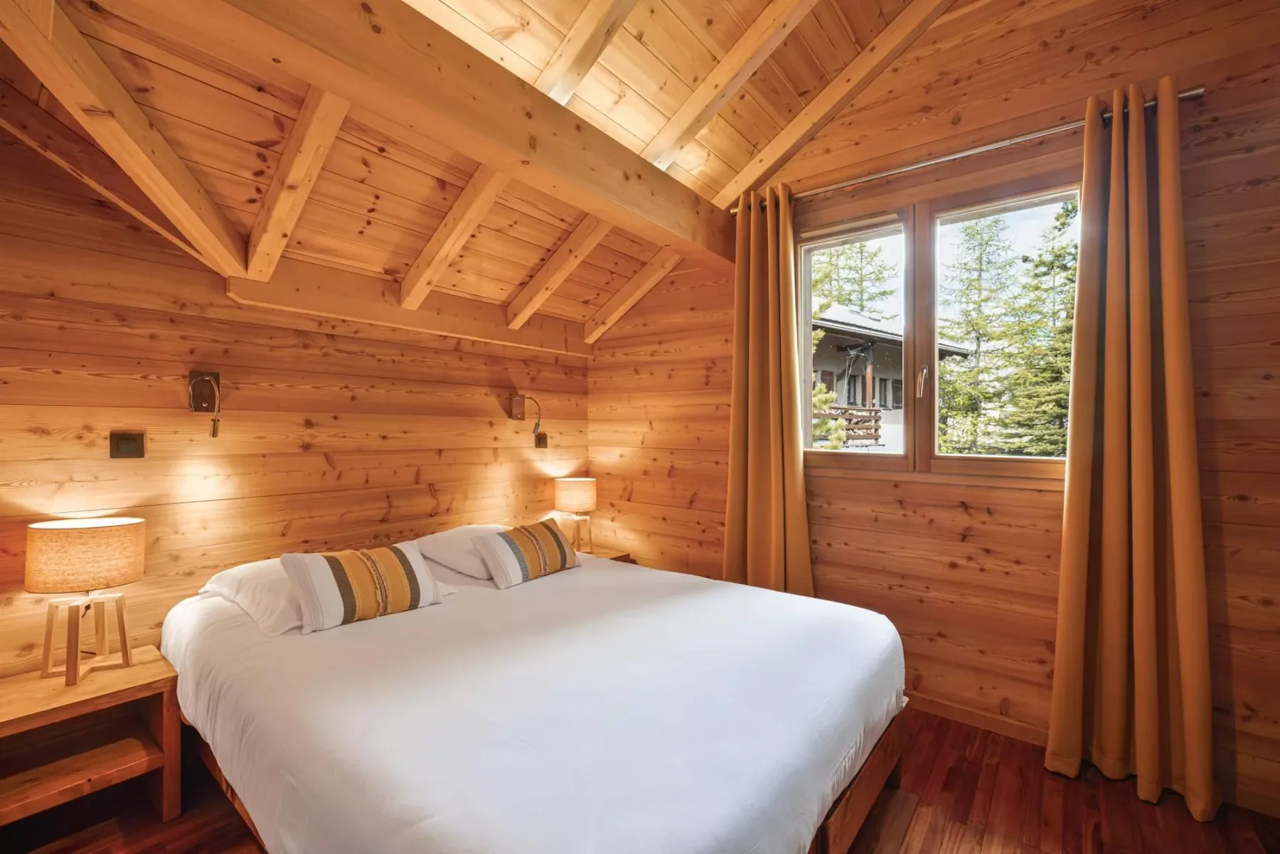 A bedroom with a large bed beneath a sloped wooden ceiling.