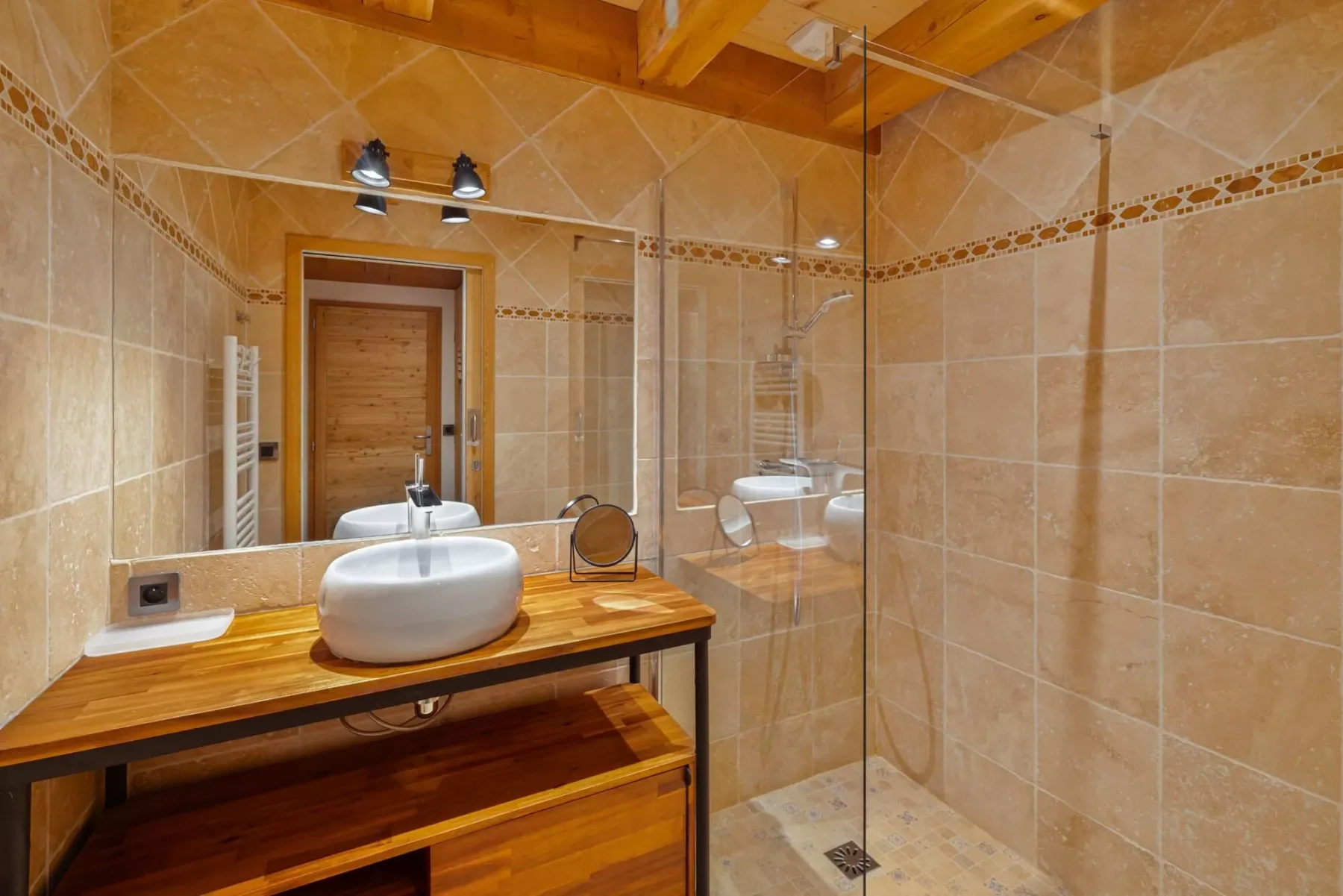 A tiled bathroom with a wooden vanity, sink, and glass shower.