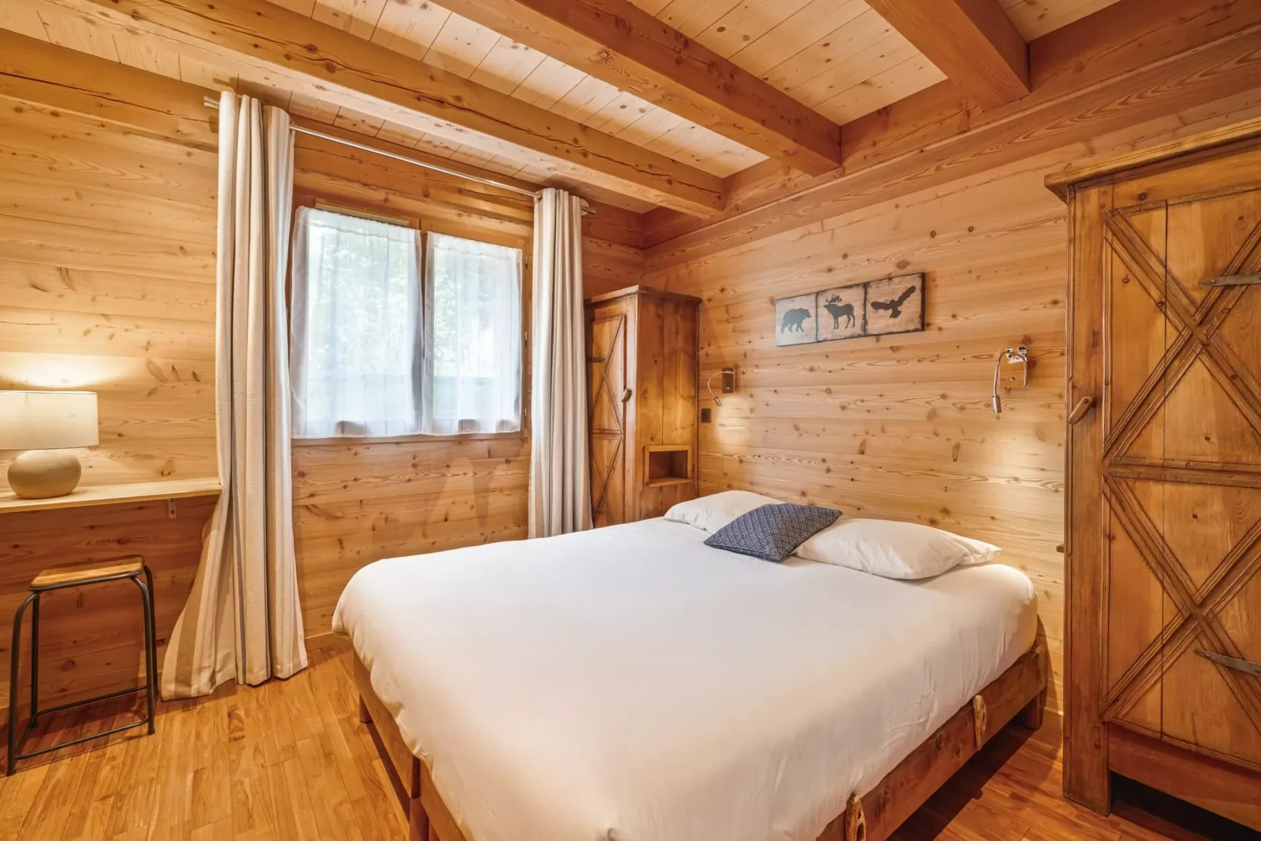 A bedroom with a large bed, wooden walls, and a curtained window.