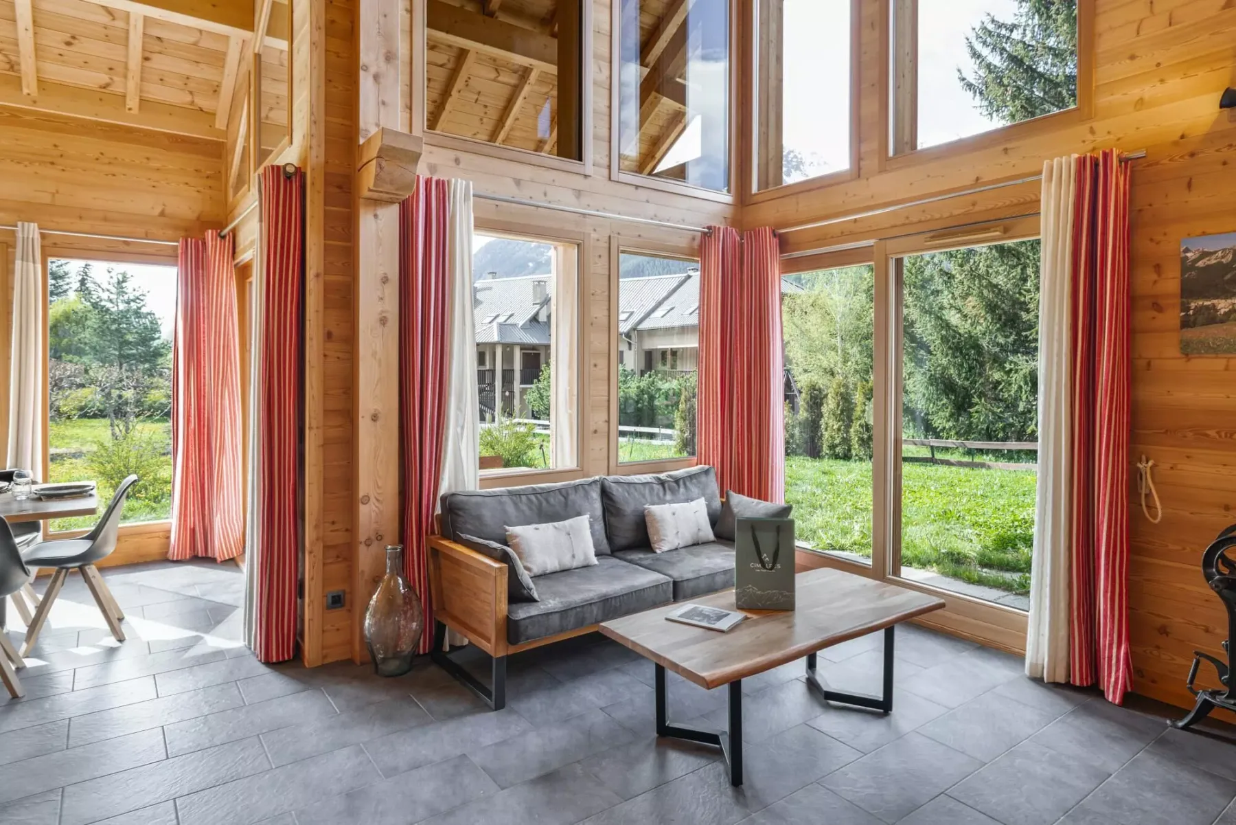 A bright living room with a gray sofa beside large windows overlooking greenery.