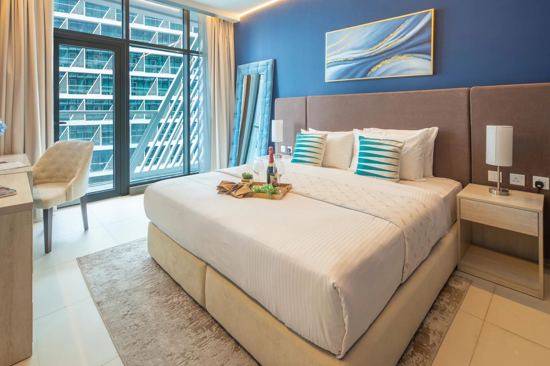 A bedroom with a large bed, blue accent wall, and floor-to-ceiling windows.