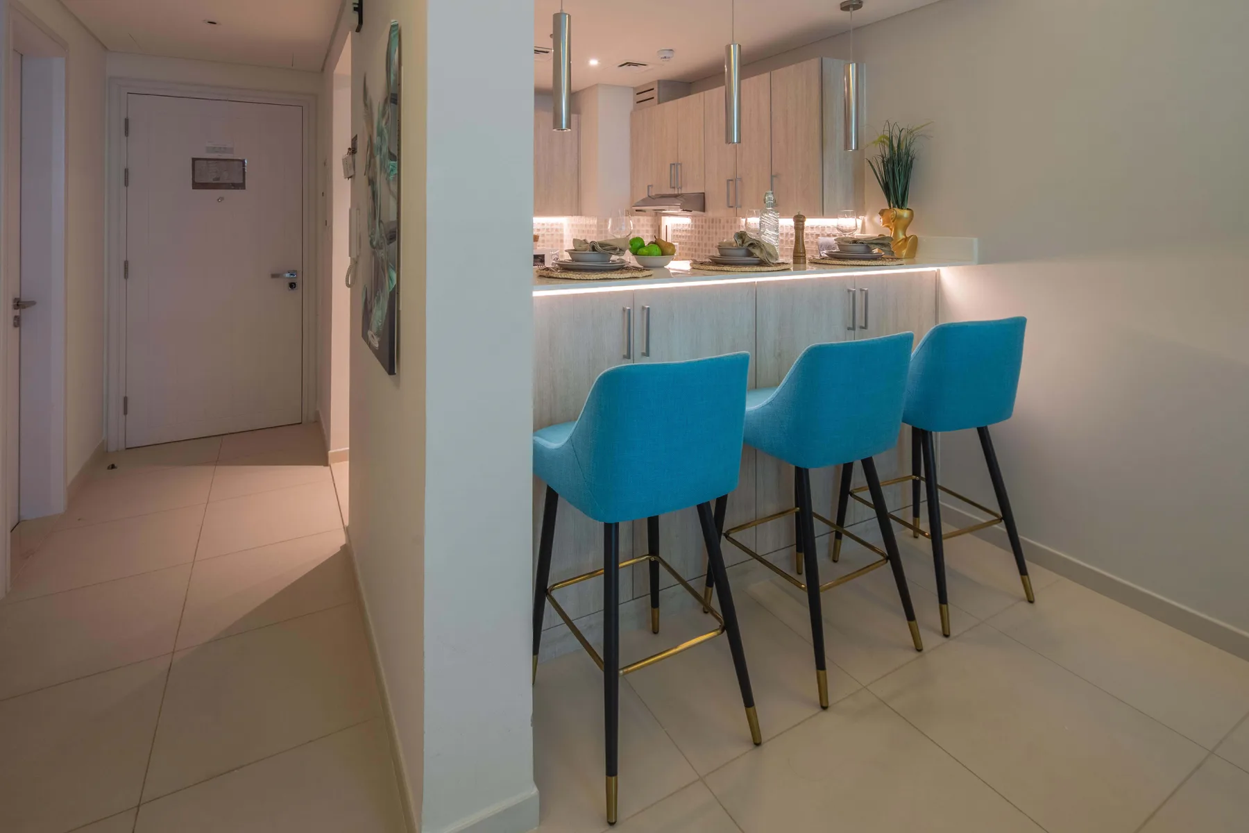A kitchen island with blue seating opens onto a tiled hallway.