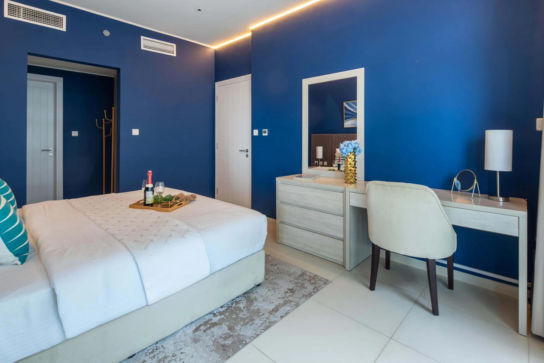 A bedroom with a large bed and a desk against a blue wall.