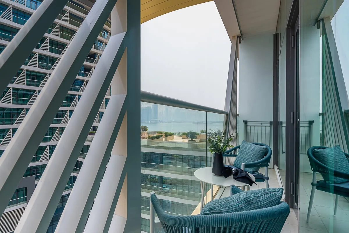 A balcony with teal seating and a glass railing overlooks the water.