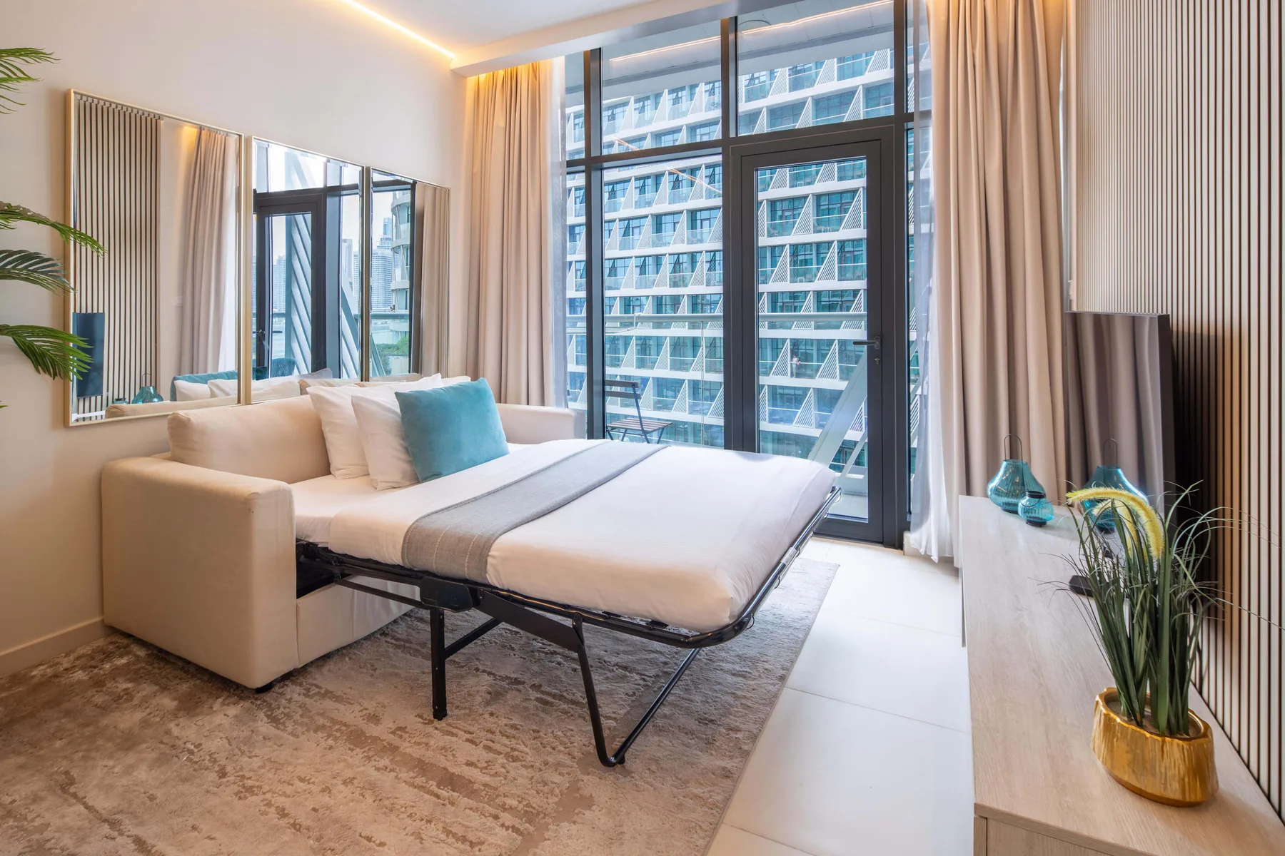A bright bedroom with a bed, a large window, and a sofa.