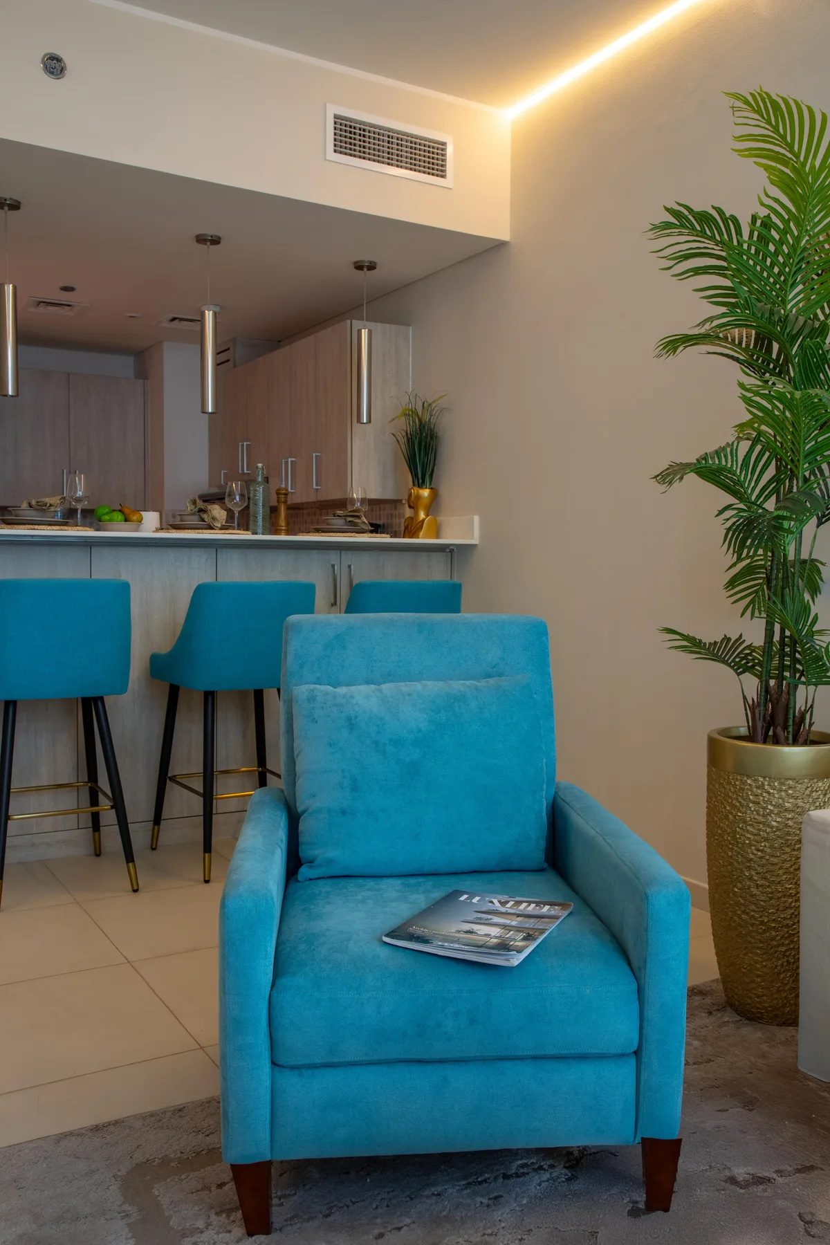 Una sala luminosa con asientos azules junto a una barra de cocina y una planta en maceta.