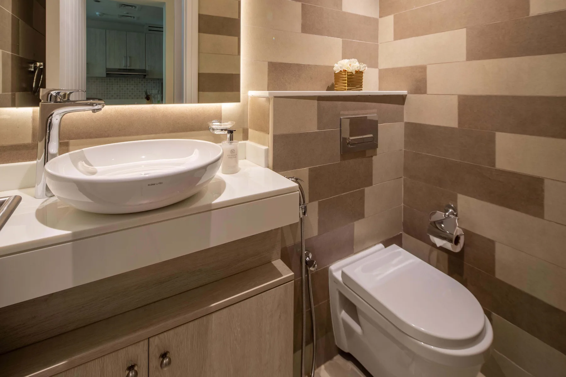 A bathroom with a sink vanity and toilet against tiled walls.
