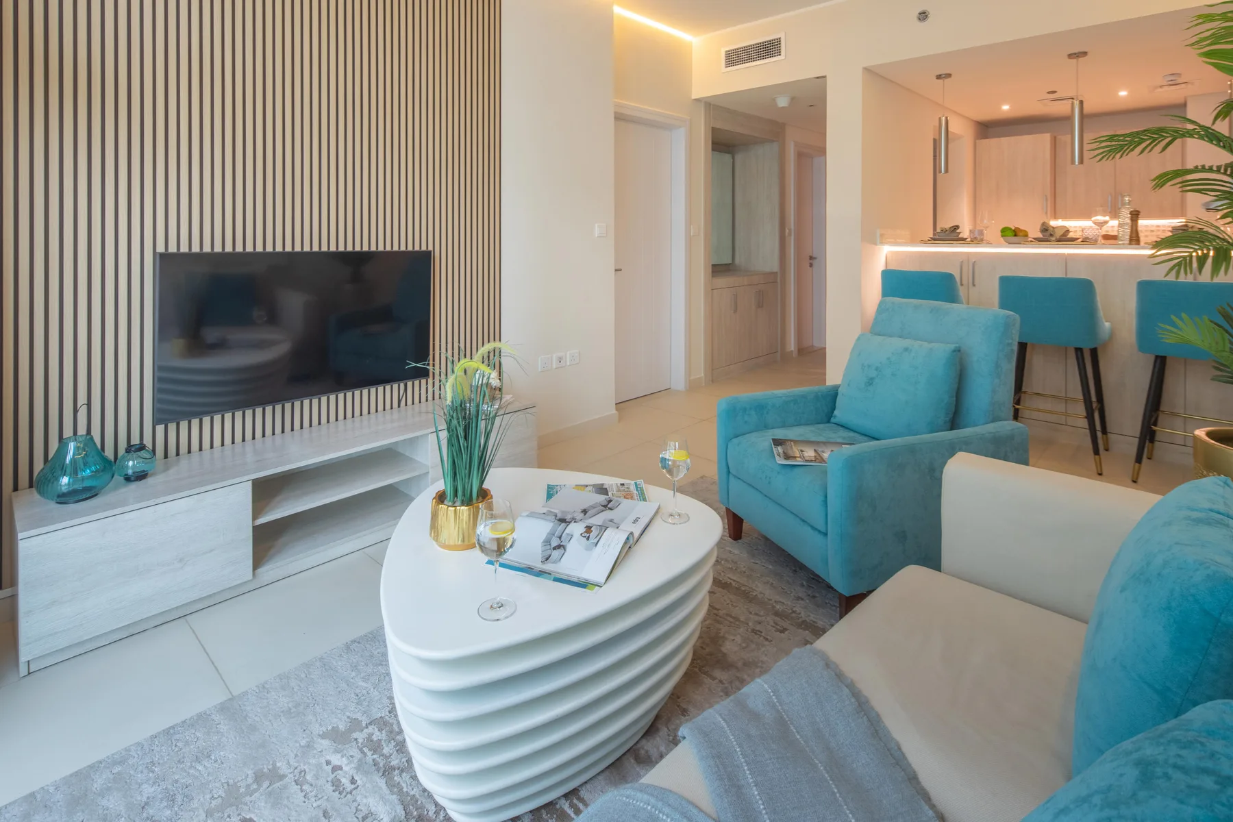 A living room with turquoise seating, a television, and an open kitchen.