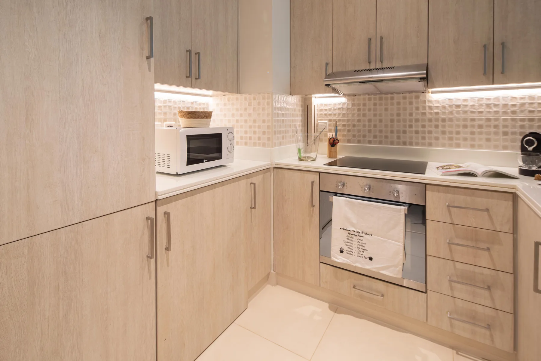 A modern kitchen with light wood cabinets, a microwave, and an oven.