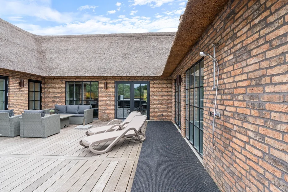An outdoor patio with lounge seating and glass doors beside a brick wall.
