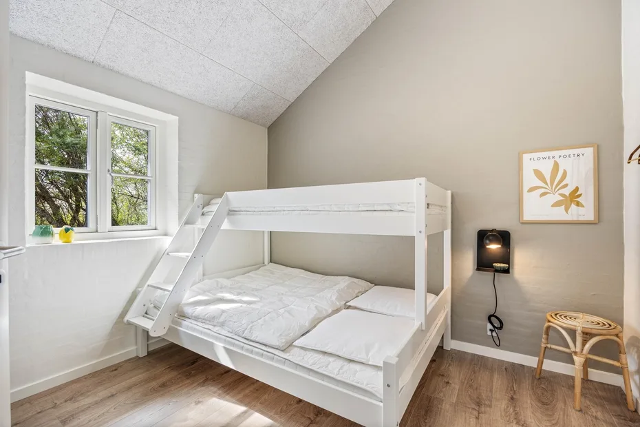 A bedroom with a white bunk bed beside a window.