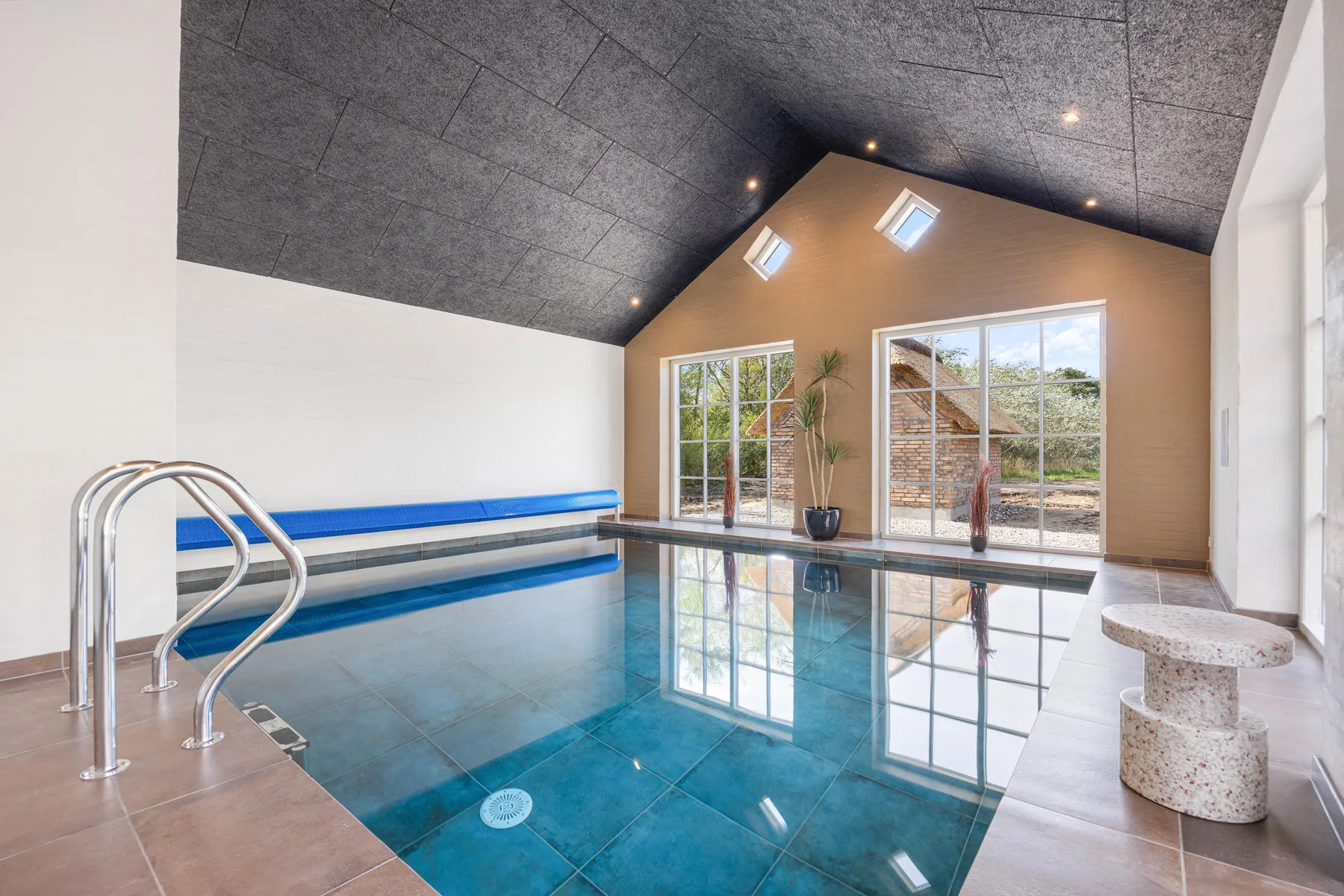 Indoor swimming pool with large windows and a high, sloped ceiling.