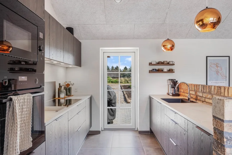 A modern kitchen with light cabinetry, a central glass door, and pendant lights.