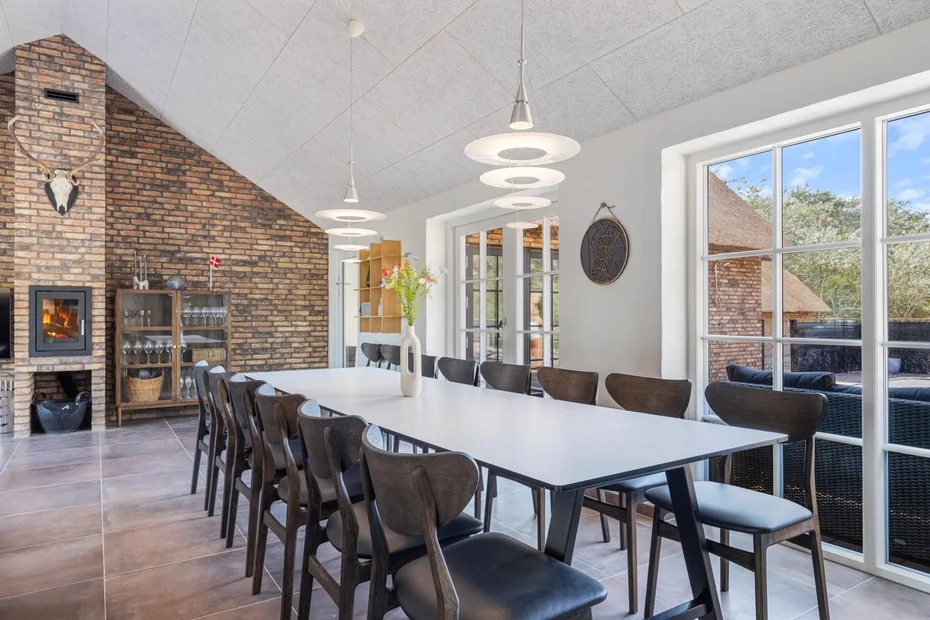 A dining room with a long table and chairs beside a brick fireplace.