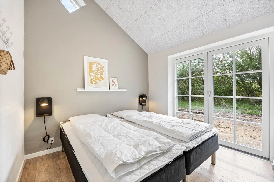 Bedroom with two beds beneath a sloped ceiling and beside large windows.