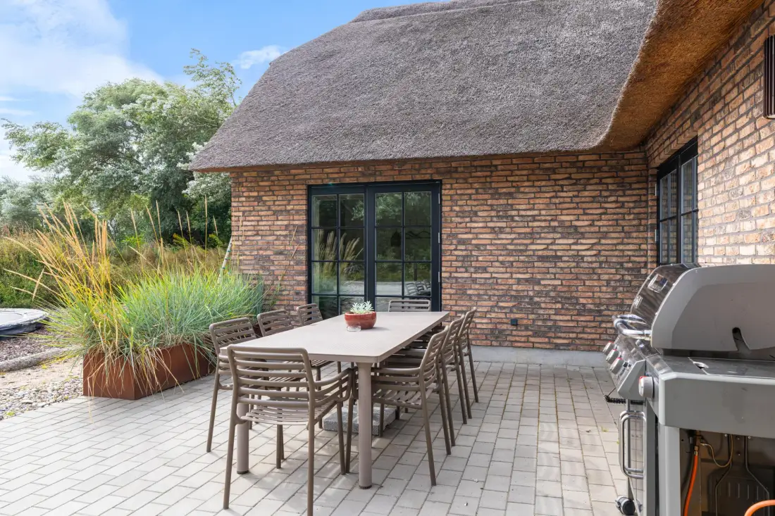 A paved outdoor dining area beside a brick building, with a table and barbecue.