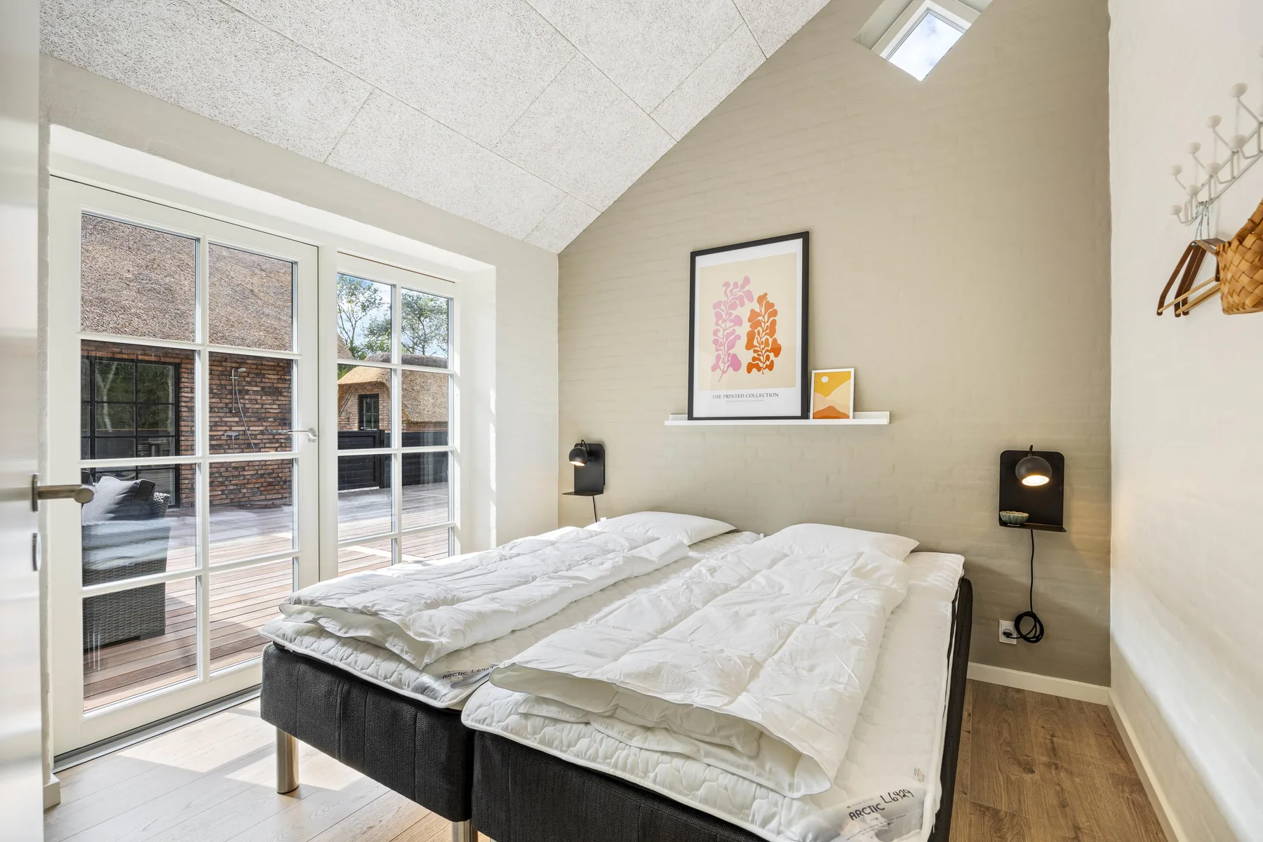 A bright bedroom with two beds beside large glass doors.