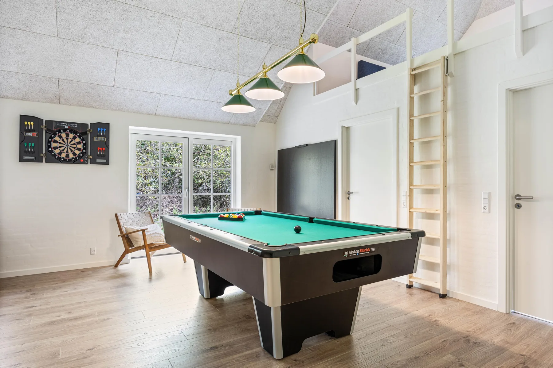 A recreation room with a pool table, dartboard, and windows.
